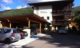 A guesthouse named "Haus Nadia" in a tranquil setting. Several cars are parked in the driveway, surrounded by green mountains.
