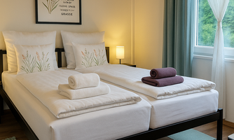 A modern bedroom with a double bed, white bedding, and decorative pillows. Large windows let in plenty of light, and the walls are stylishly decorated.