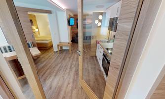 A modern room with wooden flooring and elegant furnishings. On the left side, a sleeping area can be seen, while the kitchen is visible on the right side.