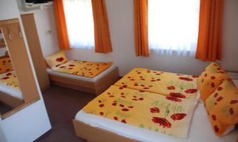 A cozy bedroom with two beds and orange curtains. The bed linen is floral and adds color to the room.