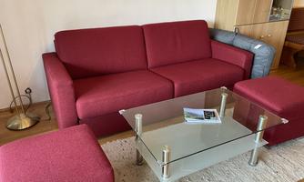 A red sofa is situated in a living area, complemented by a glass table and several stools. The room appears modern and inviting.