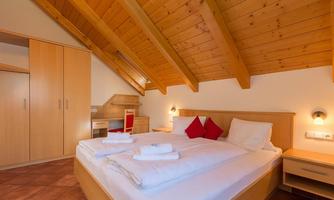 Cozy bedroom with wooden beam ceiling. The room is equipped with a double bed, two red pillows, and a desk.