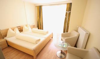 A bright and modern hotel room with a double bed and two armchairs. Large windows provide plenty of daylight and a pleasant view.