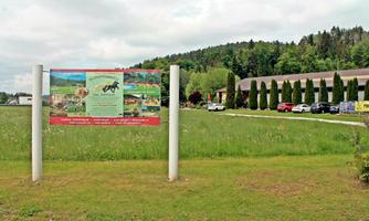 A large advertising sign for a riding stable stands on a green meadow. In the background, trees and buildings can be seen.