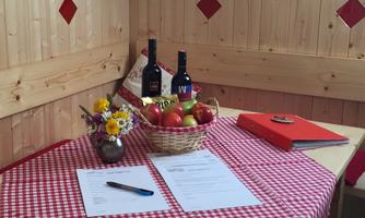A set table with a checkered tablecloth. A fruit bowl with apples, two bottles of wine, and a beautiful bouquet of flowers are decorated.