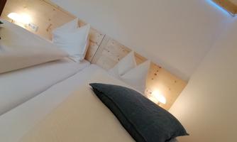 A cozy bedroom with two beds and pillows. The walls are light and accentuated with soft lighting.