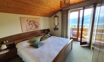 A bright bedroom with a large bed and a wooden ceiling. There is a balcony with a view and a pleasant atmosphere.