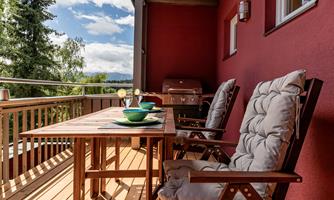 An inviting balcony with a wooden table and two comfortable chairs. Bowls are placed on the table and there is a beautiful view of nature.