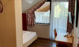 A cozy room with a window and wooden floor. There is a bed, a desk, and a clothes rack.