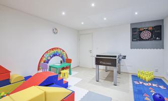A colorful play area with various play equipment, including a foosball table and soft cushions. The room is bright and modern in design.