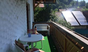 A cozy balcony with a table and two chairs. In the background, solar panels and green trees are visible.