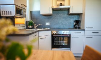 Modern kitchen with white cabinets and a stainless steel sink. A stove with oven and a coffee machine are visible.