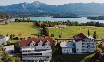 A picturesque landscape with a clear lake, surrounded by mountains. In the foreground, there are modern buildings with a swimming pool and green meadows.