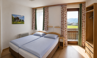 A light-filled bedroom with a double bed that can be separated into 2 single beds upon request and a beautiful view of the mountains. The decor is simple and cozy, with wooden details and floral curtains. Access to the balcony.