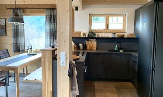 A modern kitchen with black furniture and wooden paneling. The dining area with a table and chairs is well-lit and invites you to linger.