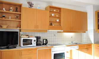 A bright kitchen with wooden cabinets and modern appliances. On the countertop are a microwave, a coffee machine, and dishes.