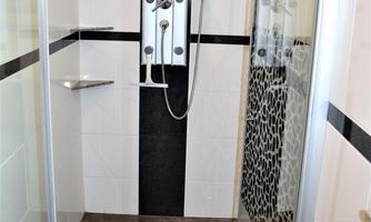 A modern shower with glass walls and various shower options. The floor is equipped with dark tiles and a non-slip mat covering.