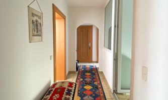 A spacious hallway with bright walls and a colorful carpet. On the left side, there is a chest and several doors lead to different rooms.