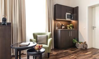 A modern kitchen with hardwood flooring and a cozy armchair. Apples are on the table and a plant is on the countertop.