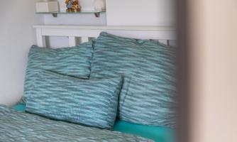 A cozy bed with pillows in soft shades of blue and green. Decorative elements are visible in the background.