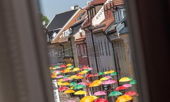 A colorful street with many sun umbrellas in different colors. People are strolling through the picturesque scenery.