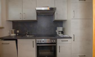 A modern kitchen with gray cabinets and a stainless steel stove and oven combination. There is a small sink and additional kitchen appliances on the countertop.
