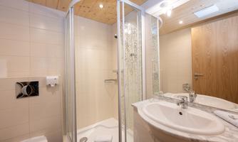 A modern bathroom with a shower and sink. The walls are brightly tiled, and there are wood paneling on the ceiling.