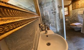 A modern bathroom with a sink and a large mirror. The walls are clad with gray stones and there is a shower.