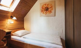 A cozy room with a single bed and wooden paneling. On the wall, there is a picture of a sunflower and a window lets in natural light.
