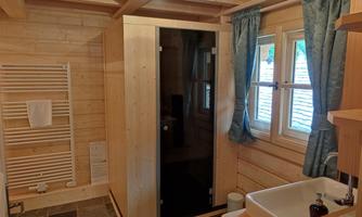 A cozy bathroom in a wooden house with a shower and a built-in sink. Large windows provide plenty of daylight and a pleasant atmosphere.