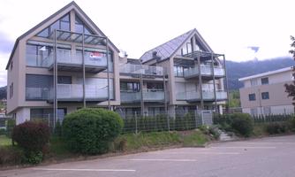 Modern residential buildings with large terraces and balconies. In the background, gentle hills can be seen.