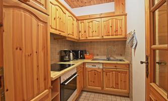 A small kitchen with wooden cabinets and beige tiles. It is well-equipped with a stove, a sink, and kitchen appliances.