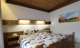 A cozy bedroom with a wooden bed and bedding featuring animal motifs. A picture of an autumn landscape hangs on the wall.