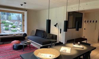A modern living space with a cozy seating area and a dining table. The room has large windows overlooking the garden and is well-lit.
