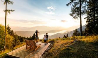 A picturesque view of the mountains and a lake at sunset. A group of people stands on a wooden platform and enjoys the landscape.