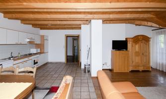 A bright, open apartment with wooden ceilings and tiled floors. The kitchen is modern and is located next to a cozy living area.