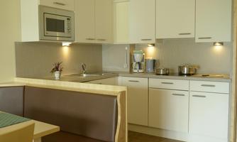 A modern kitchen with white cabinets and a bright countertop. On the countertop, there is a kettle and some pots.