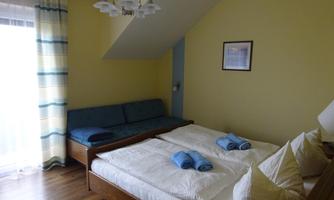 A cozy bedroom with a double bed and a sofa bed. The walls are painted yellow, and large windows provide plenty of natural light.