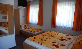 A cozy room with two beds and orange curtains. The walls are light, and a mirror reflects the interior decor.