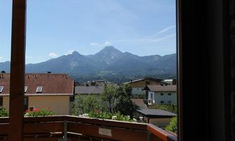 A view of the mountains from a balcony. The surroundings are green with some houses and a clear blue sky.
