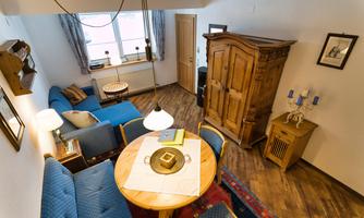 A cozy apartment with blue sofas and a round table. The room has wooden floors and a traditional cabinet is also visible.