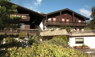A charming building with wooden cladding and balconies. Surrounded by green plants and a blue sky.
