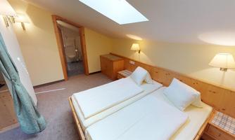 A cozy bedroom with two single beds and wooden panels. The room has a flat skylight and soft lighting.