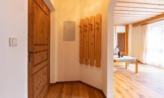 A bright and inviting hallway with wooden decor. Several coat hooks hang on the wall, and a door leads to another room.