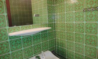 A bathroom with green tiles and a bathtub. A mirror and a shelf are visible.