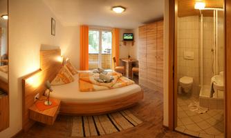 A cozy room with a round bed and wood decorations. There is a bathroom with a shower and a window that lets in natural light.