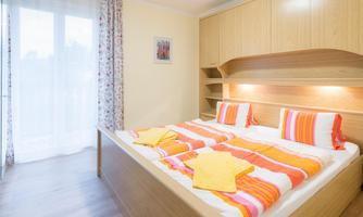 A bright and inviting bedroom with a large double bed and colorful bedding. The room has large windows that let in plenty of natural light.