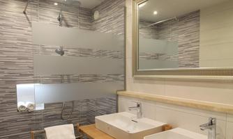 A modern bathroom with two sinks and a spacious shower. The walls are decorated with textured tiles and the room is brightly lit.