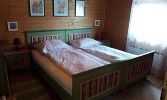 A cozy bedroom with two beds and wooden paneling. There are colorful pictures on the wall and curtains that filter the light.
