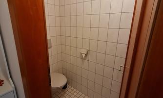 A small bathroom with tiled walls and a modern toilet. The floor is covered with square tiles.